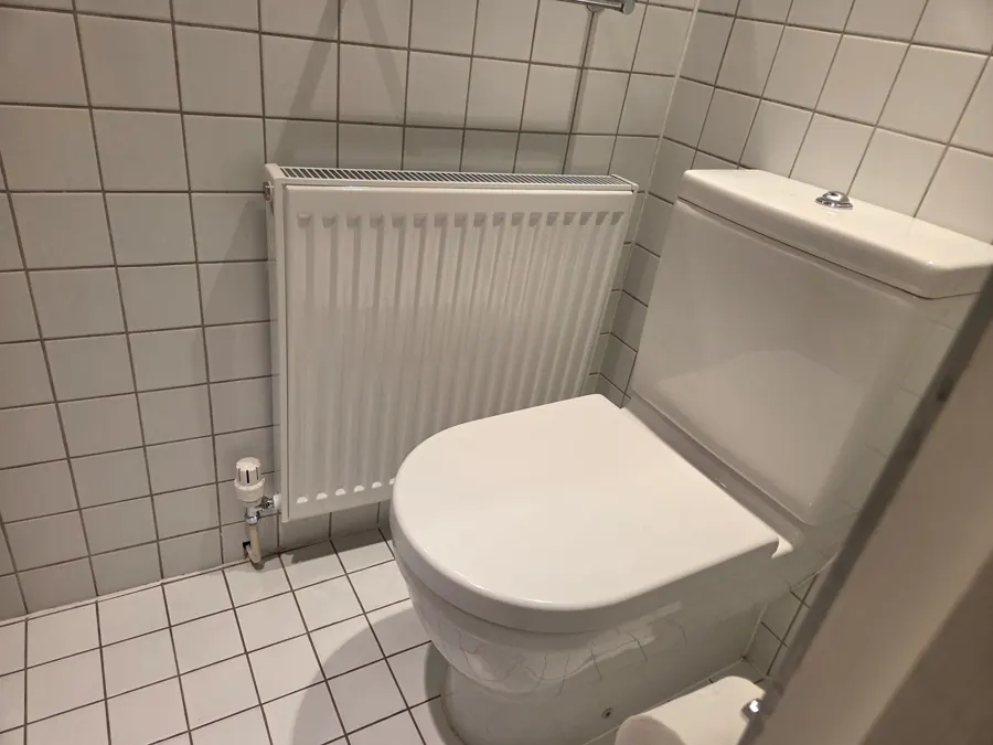 White radiator with thermostatic valve beside a toilet in a tiled bathroom