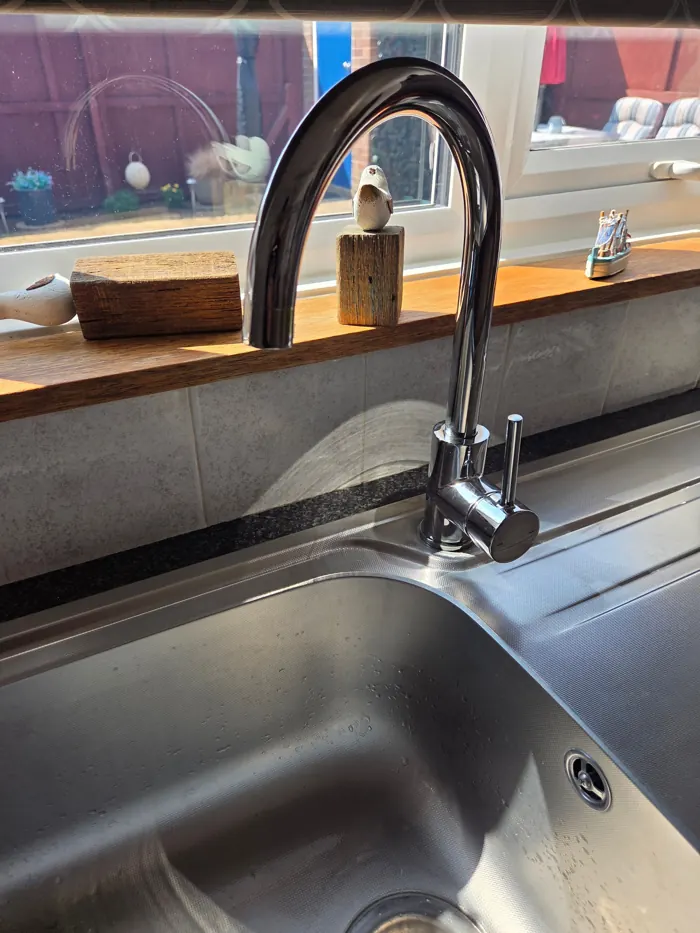 Chrome swan-neck mixer tap over a stainless steel kitchen sink